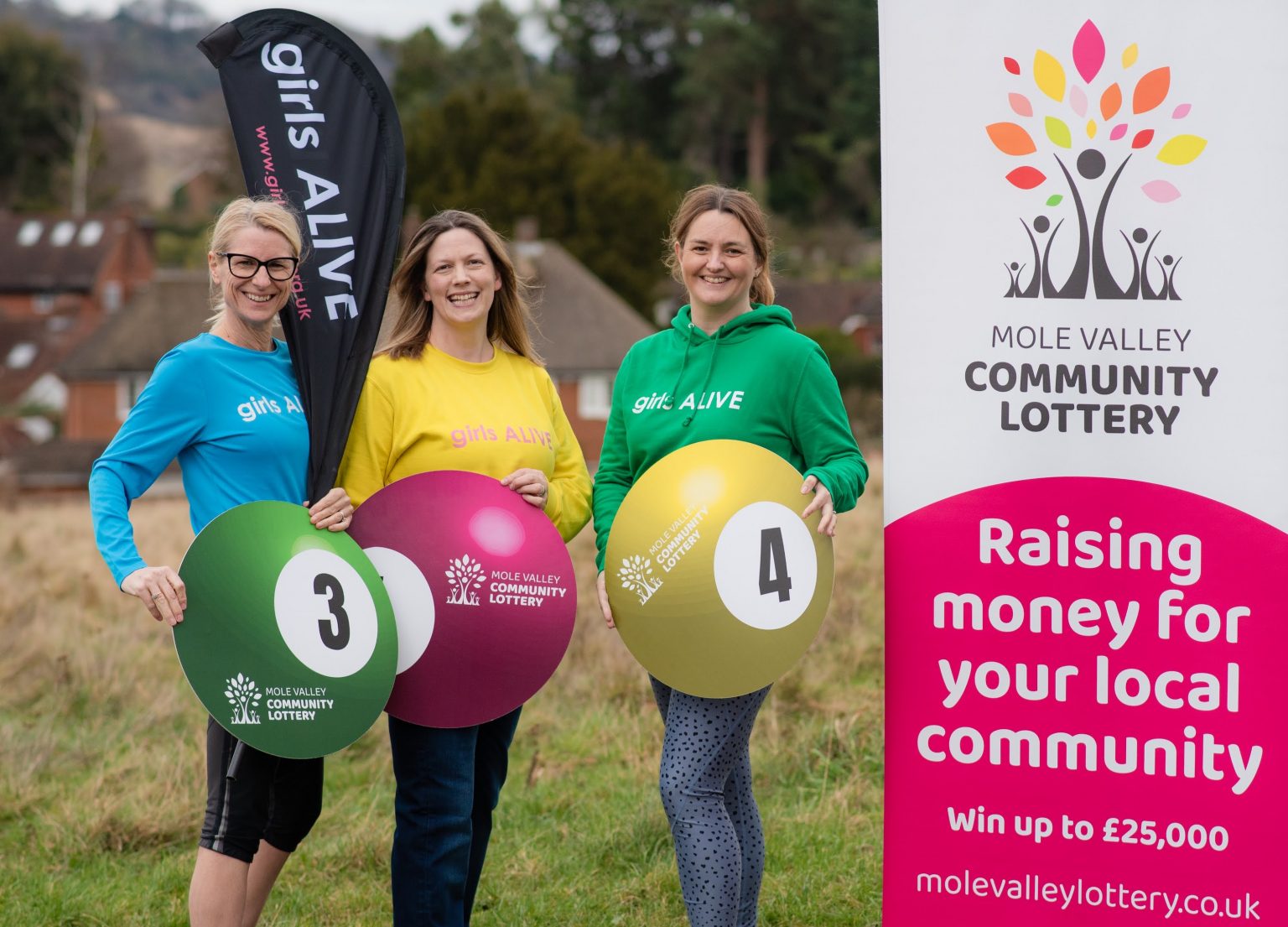 Three female representatives from Girls Alive standing with large Mole Valley Community Lottery balls.